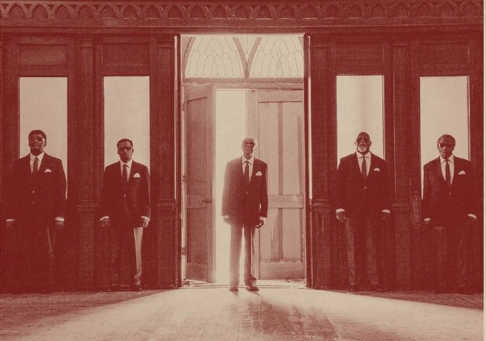 All five members of Blind Boys of Alabama standing in front of windows from inside an old church